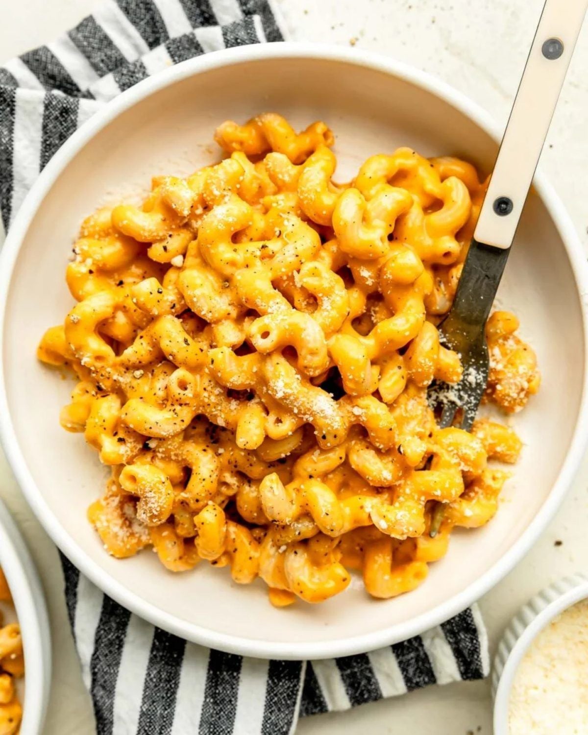 Creamy butternut squash mac and cheese in a white bowl with a fork and black pepper dusting