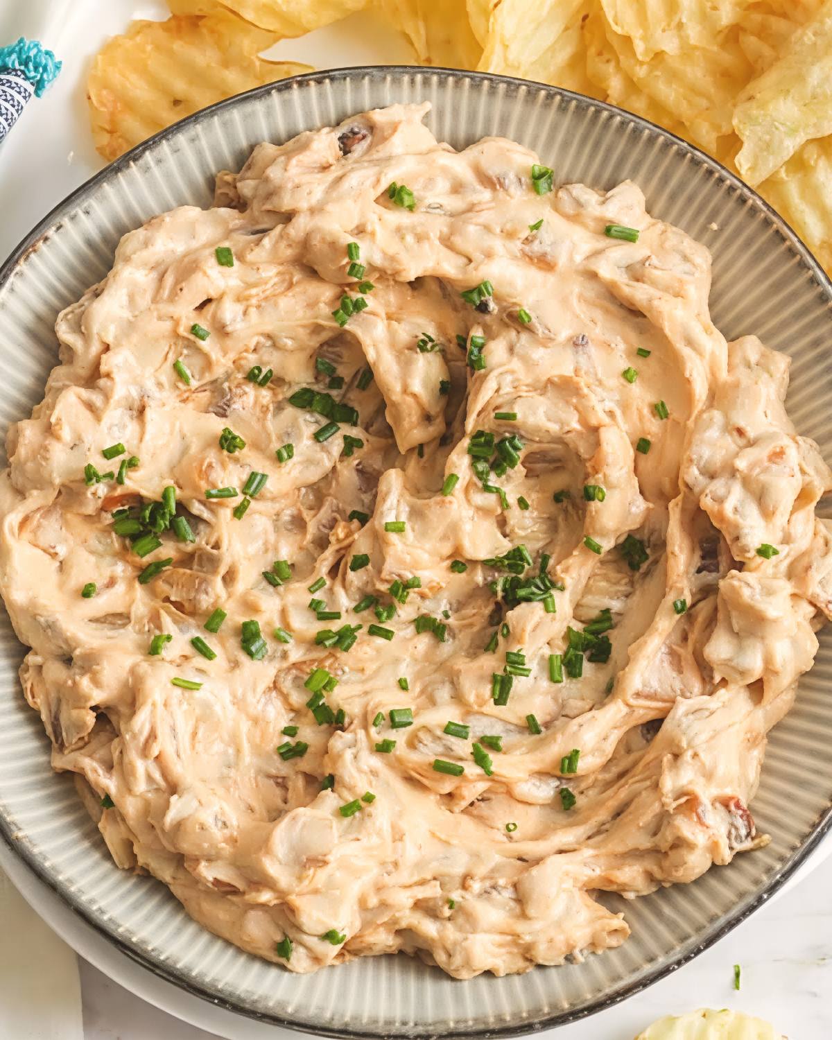 Caramelized onion fall dip in a ribbed bowl, garnished with chopped chives and served with chips.