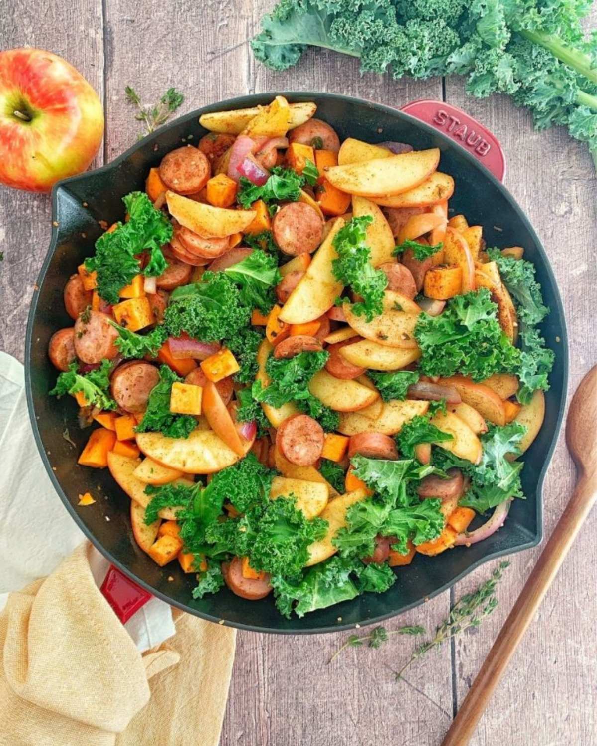 Fall skillet dinner with sliced sausage, roasted apples, sweet potatoes, and fresh kale in a Staub cast-iron pan
