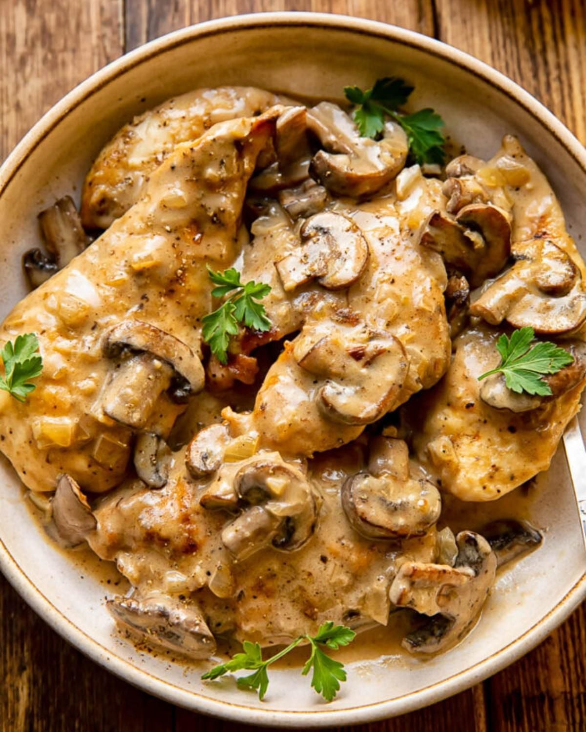 Tender poultry cutlets smothered in a rich wine reduction sauce and topped with sliced mushrooms in a shallow bowl.
