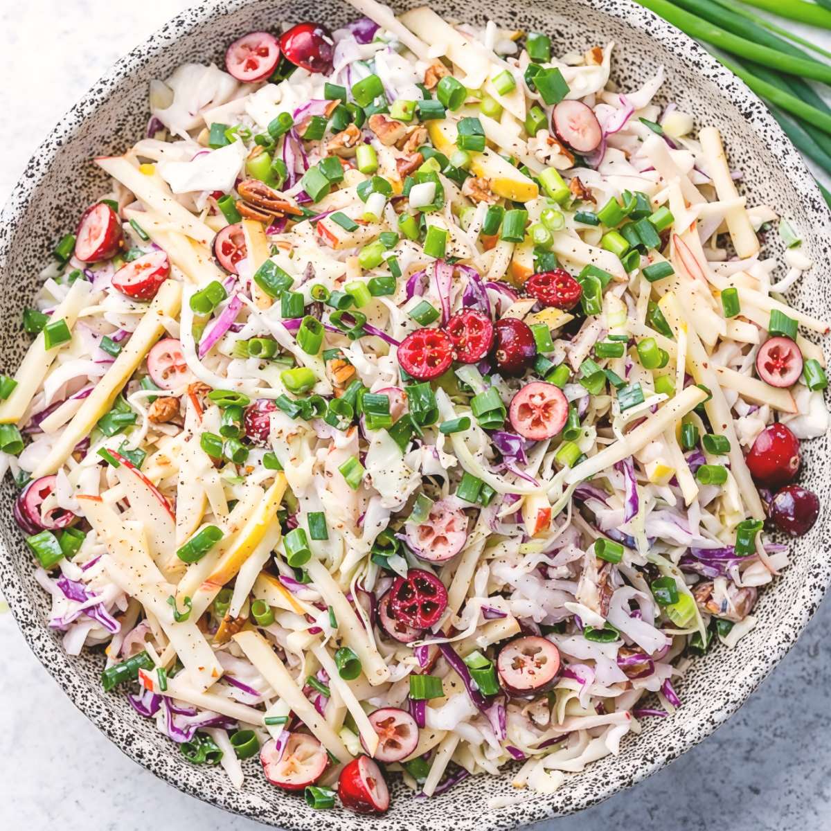 Crisp cranberry apple coleslaw tossed with chopped green onions and nuts in a textured bowl, served as a refreshing cold Thanksgiving side dish
