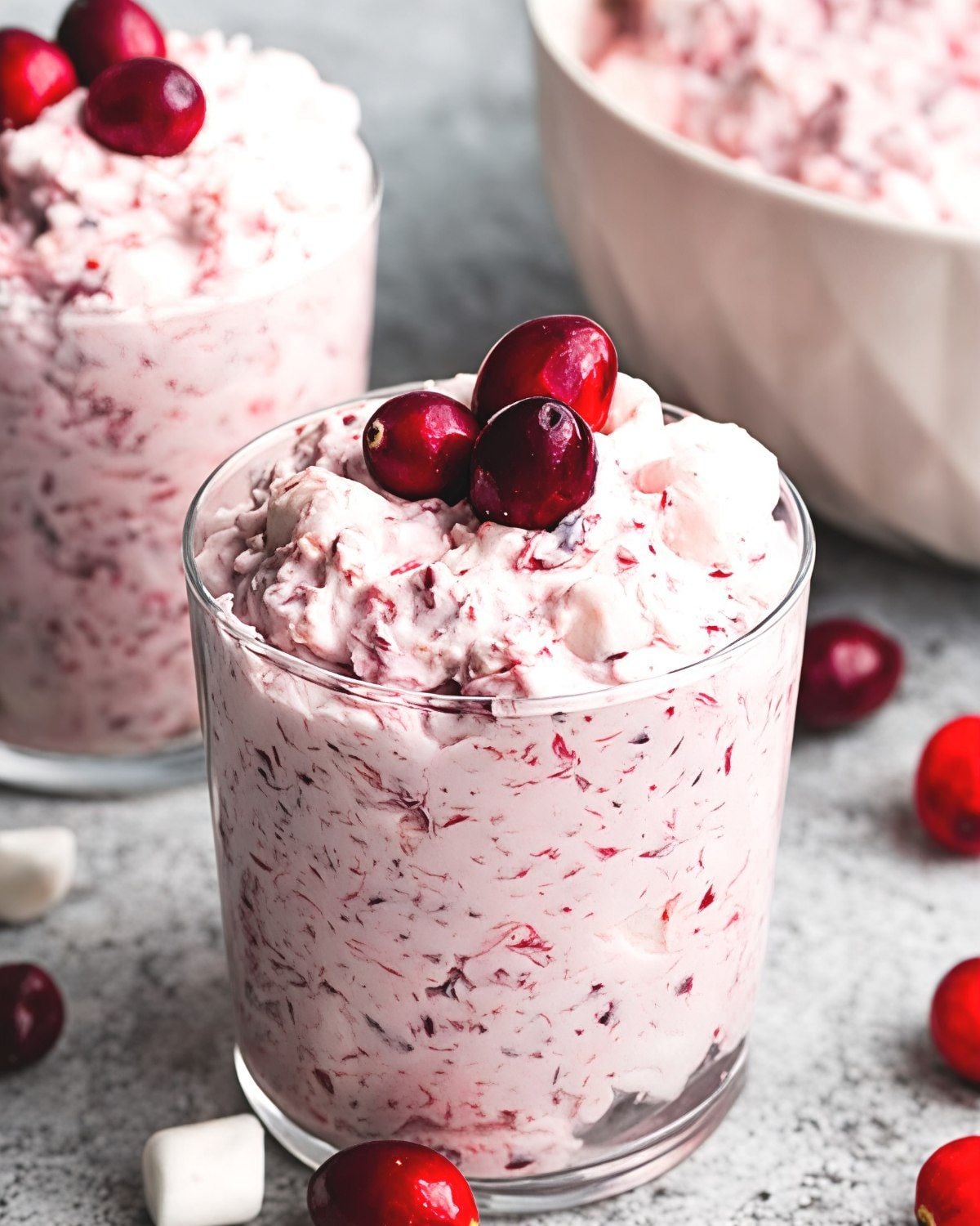 Creamy cranberry fluff salad topped with fresh cranberries in a glass, served as a refreshing cold Thanksgiving side dish.