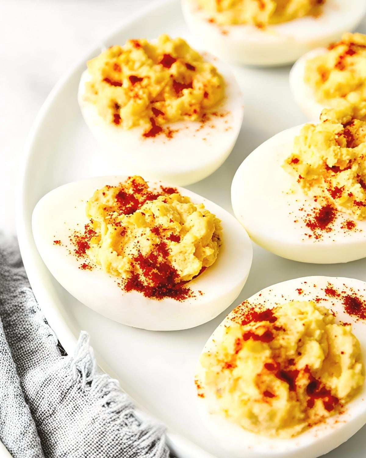 Classic deviled eggs dusted with paprika on a white platter, served as a cold Thanksgiving side dish