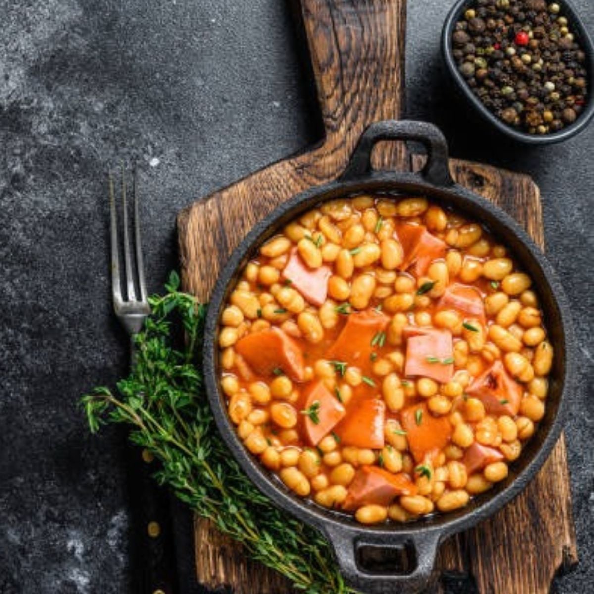 Ham and Beans in a skillet on a wooden board with fresh herbs on the side