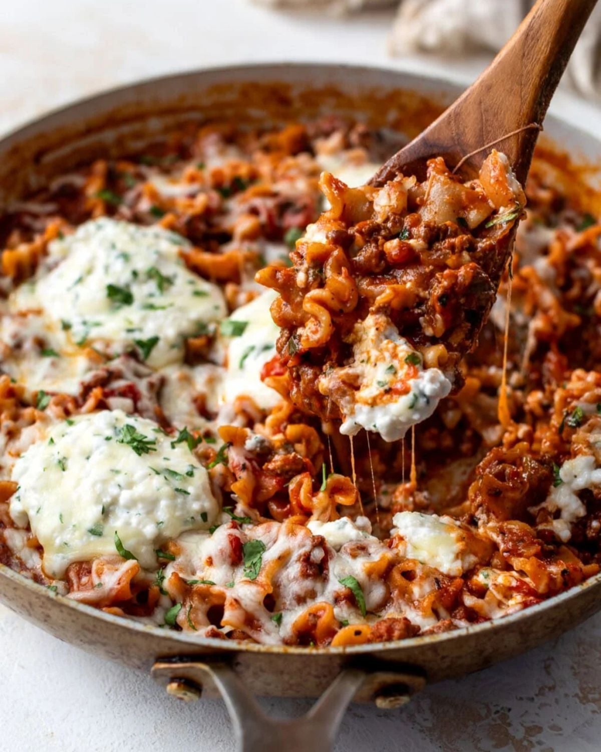 A skillet filled with pasta in a rich red sauce, topped with shredded mozzarella cheese and dollops of ricotta cheese.