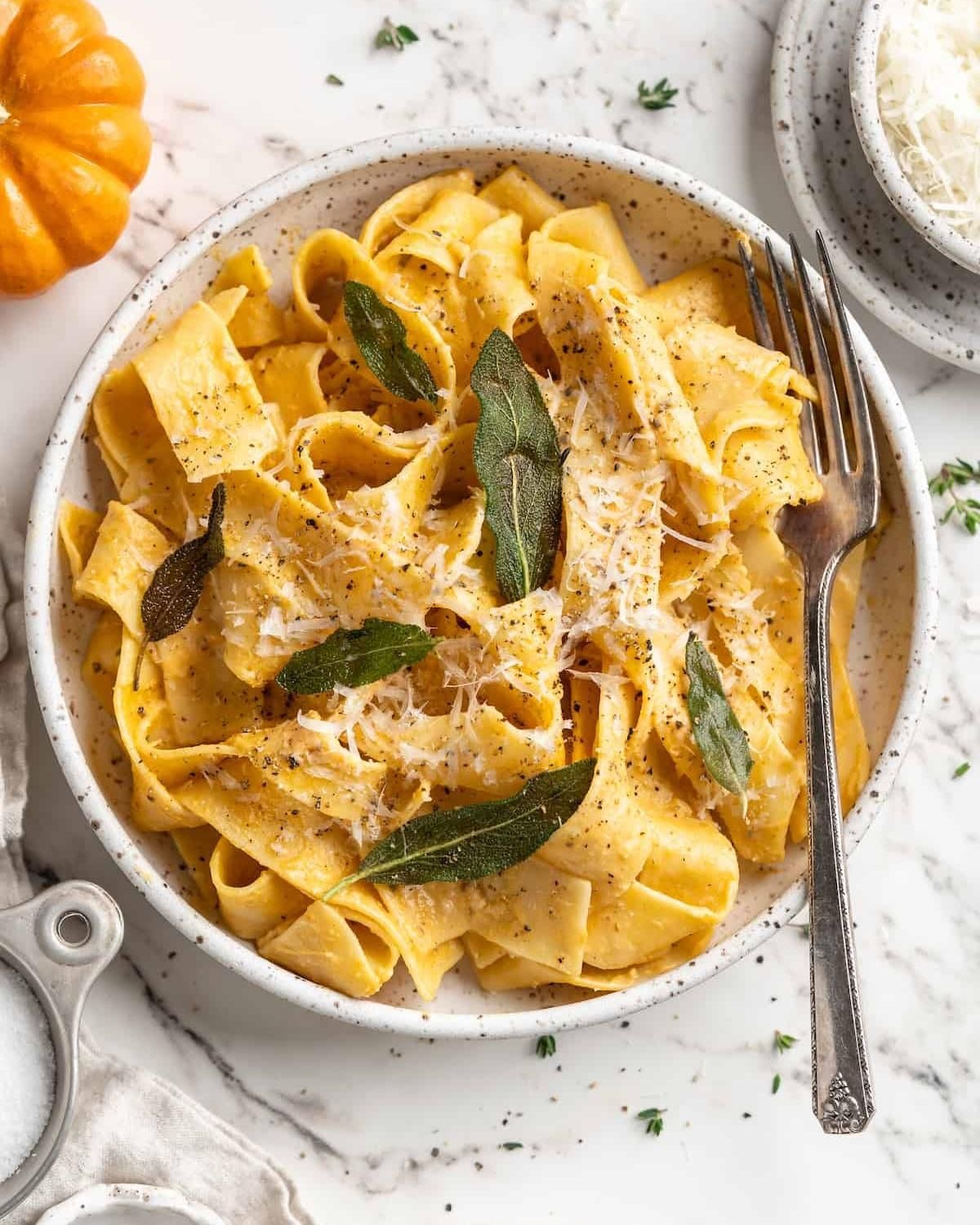 Wide ribbon noodles coated in a rich autumn squash sauce, garnished with grated cheese and fried herb leaves in a bowl.