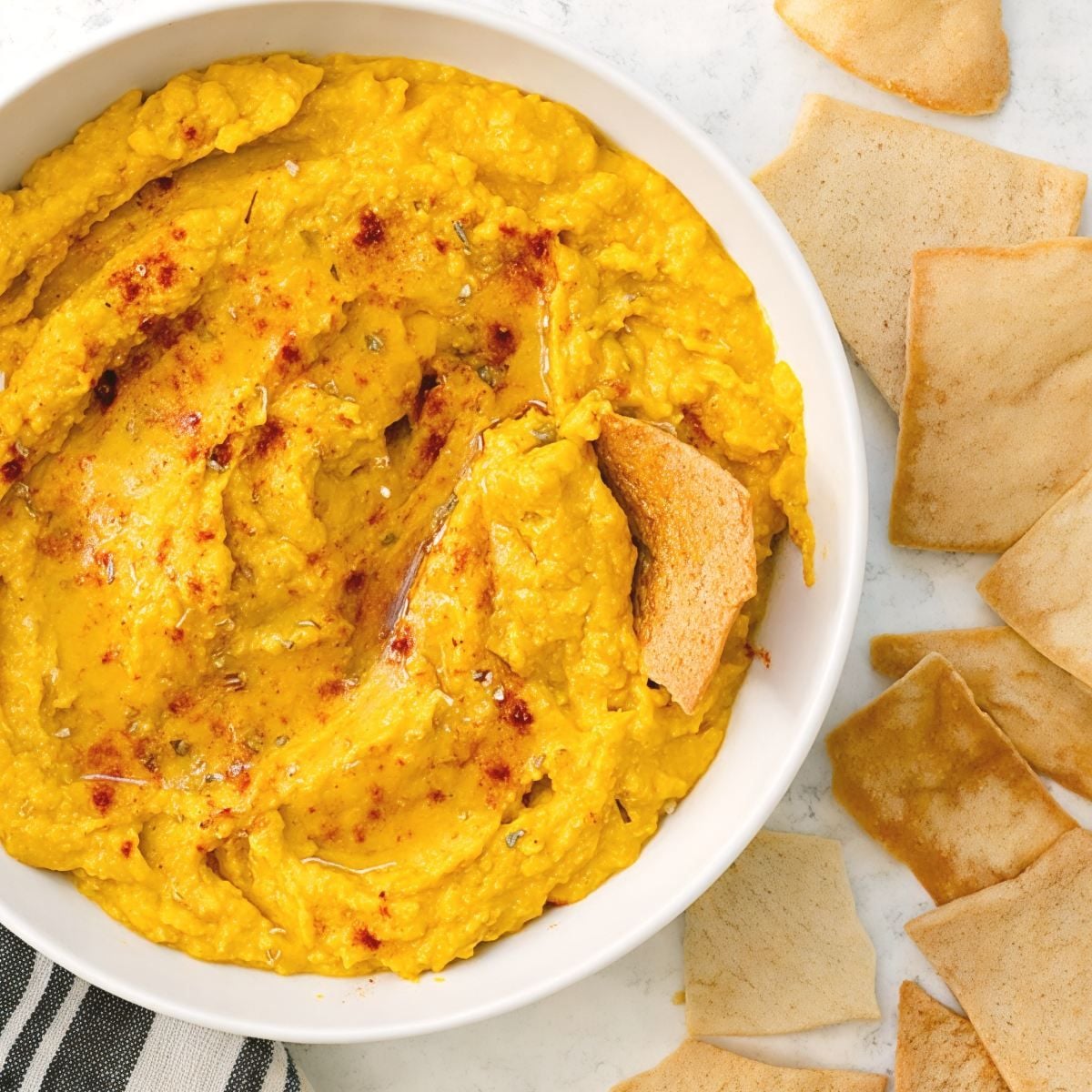 Creamy pumpkin hummus fall dip dusted with paprika in a white bowl, served with pita chips.