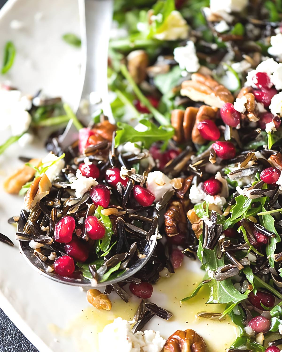 Wild rice salad with pomegranate seeds, greens, and nuts being scooped with a spoon as a unique Thanksgiving side dish