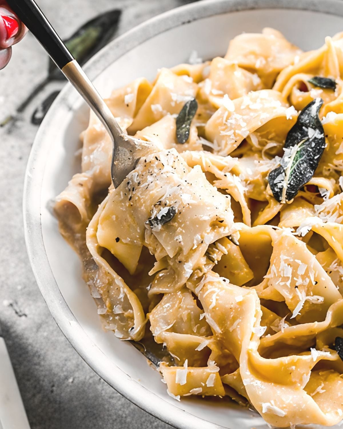 A fork twirling roasted butternut squash pasta in a white bowl, topped with grated cheese and crispy sage leaves for an easy fall dinner.