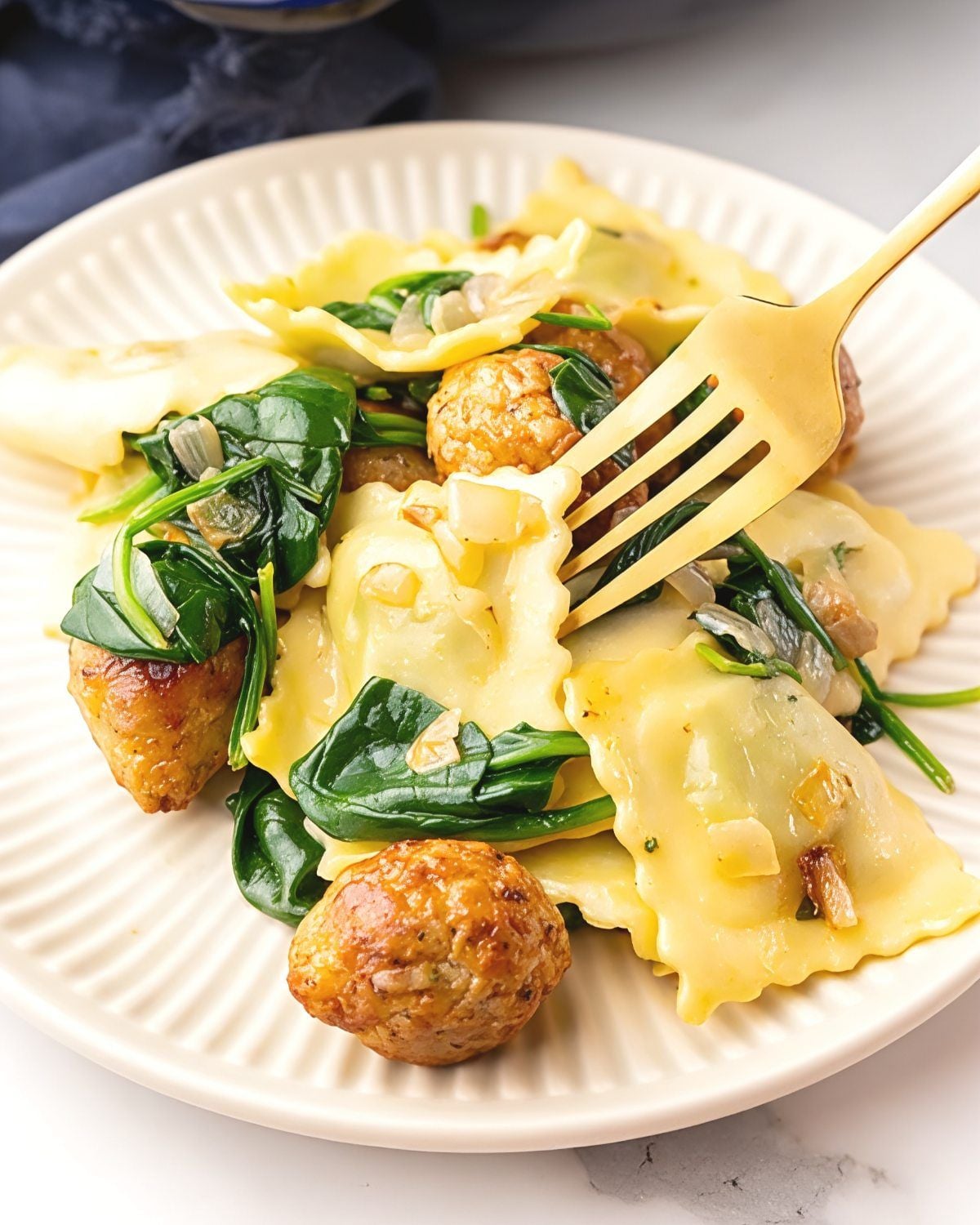 A plate of sausage meatball skillet ravioli tossed with fresh spinach and a golden fork, making an easy fall dinner.