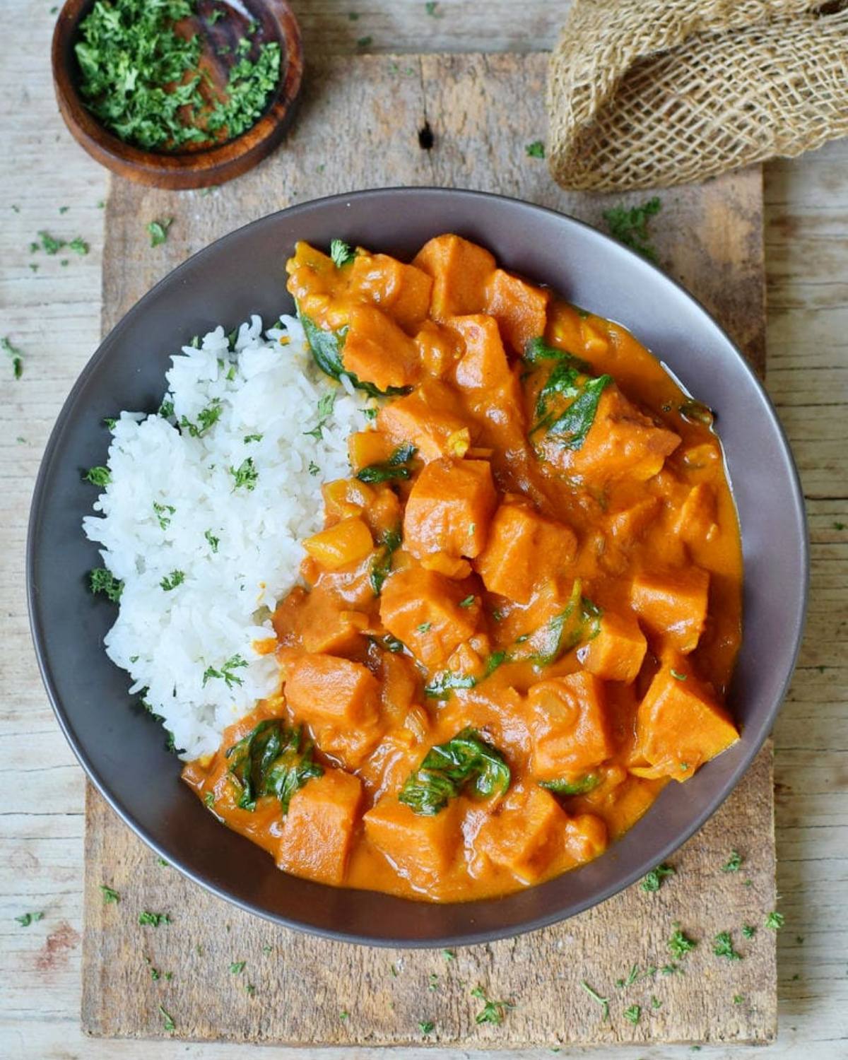 Orange root vegetable curry and dark leafy greens served next to a portion of white rice in a dark bowl.