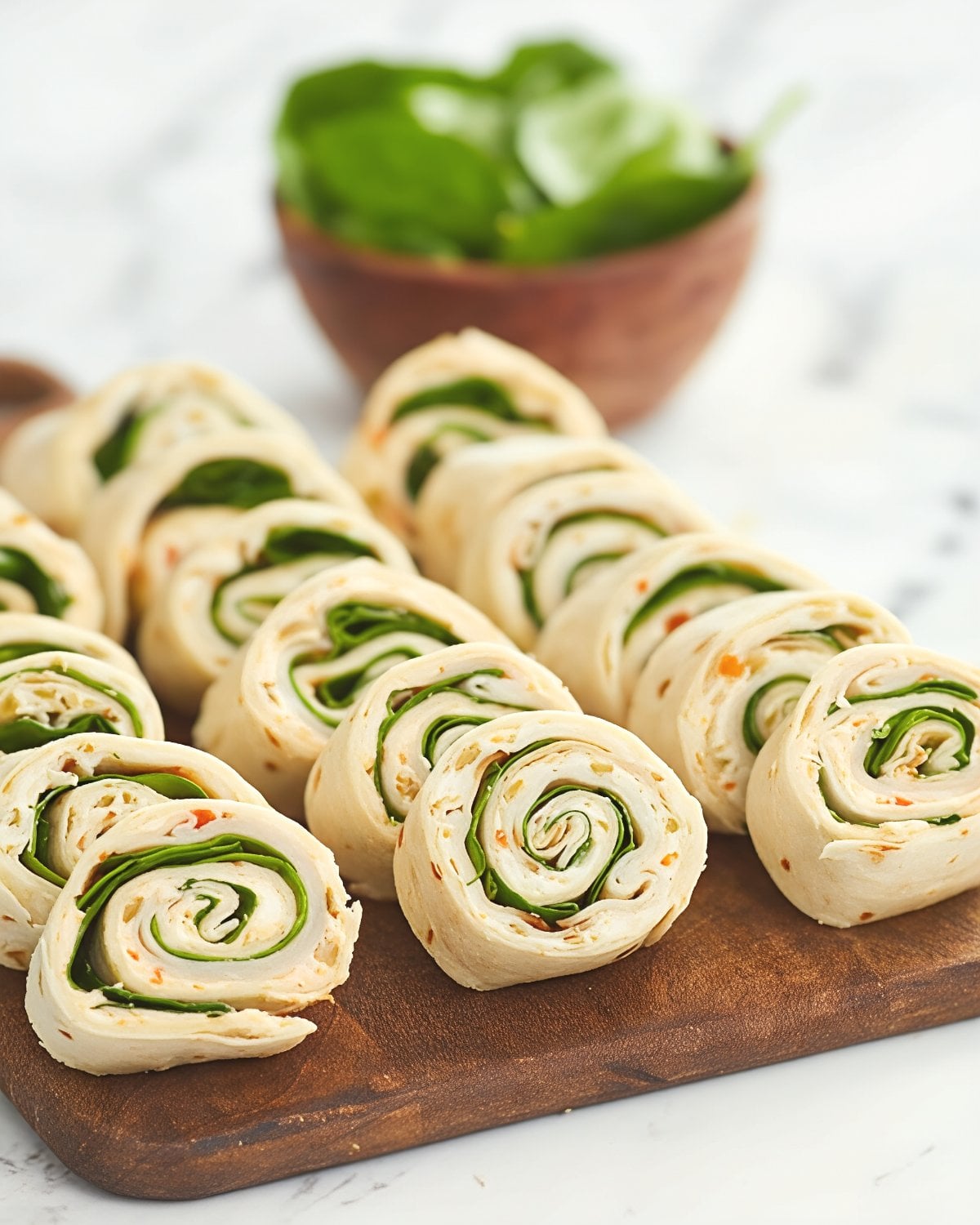 A wooden cutting board lined with sliced turkey pinwheels rolled up in tortillas with layers of cream cheese, turkey, and fresh green spinach.