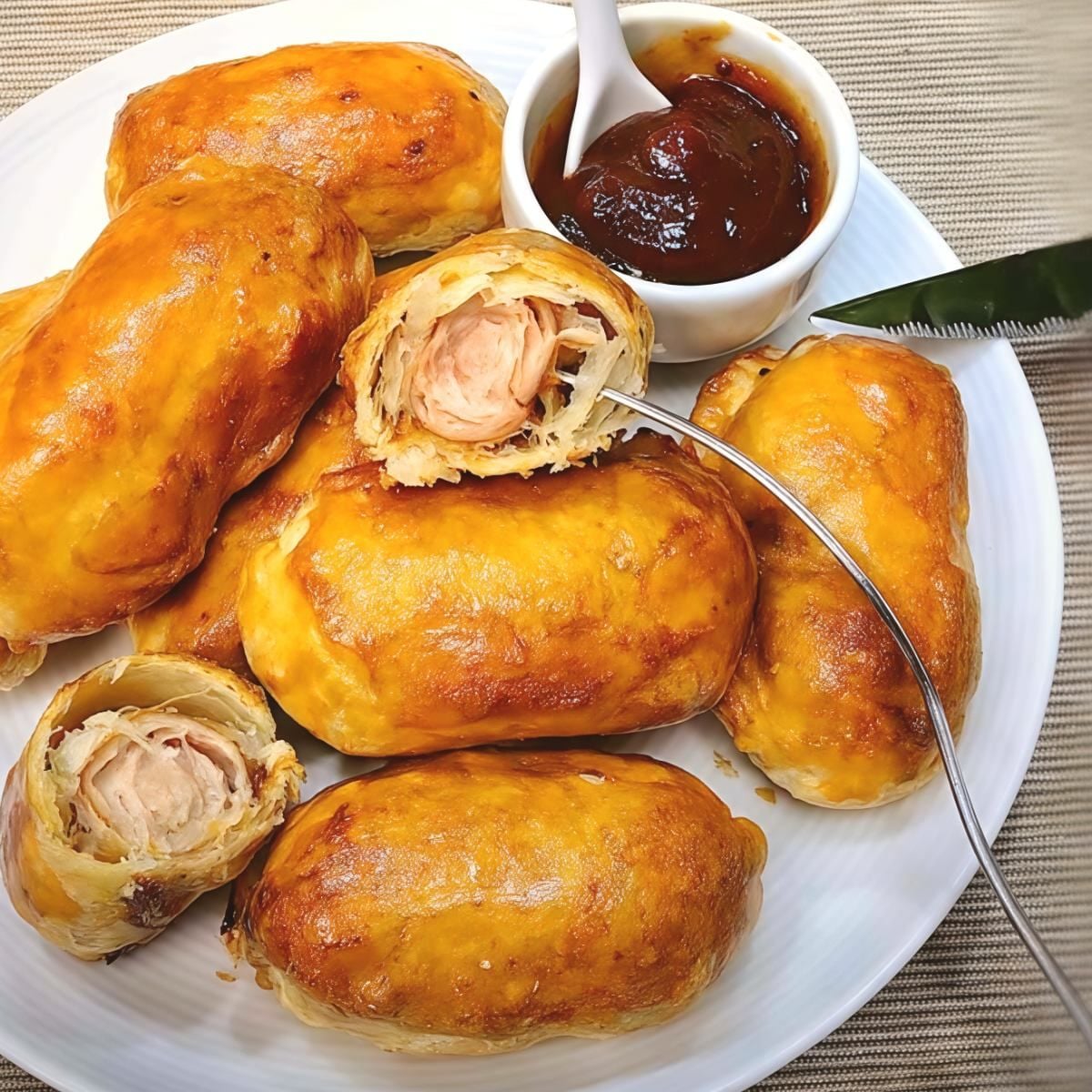 Golden brown air fryer sausage rolls served on a white plate with a small bowl of dipping sauce.