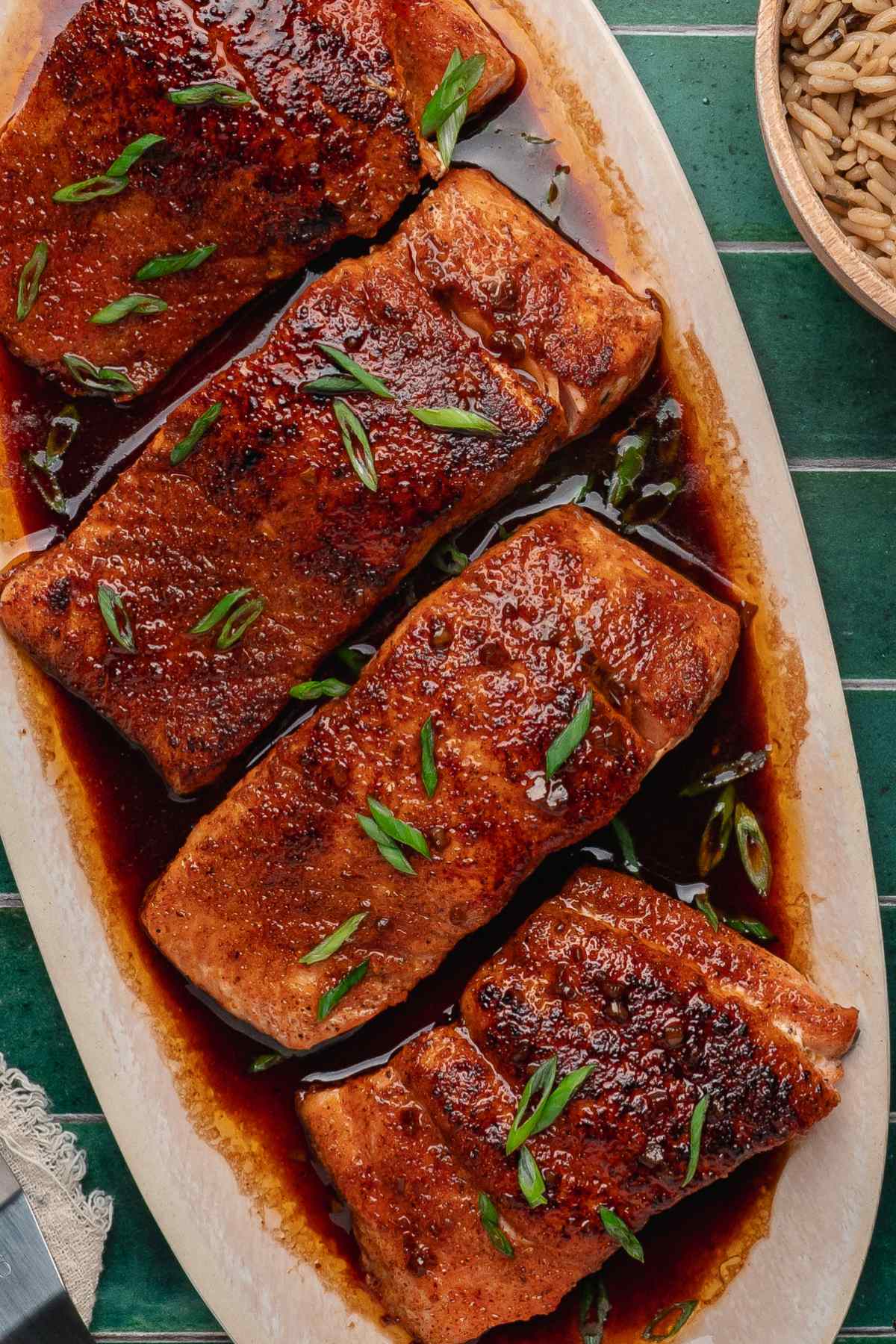 Bourbon glazed fish portions drizzled with a rich sauce and topped with sliced green onions on an oblong platter.
