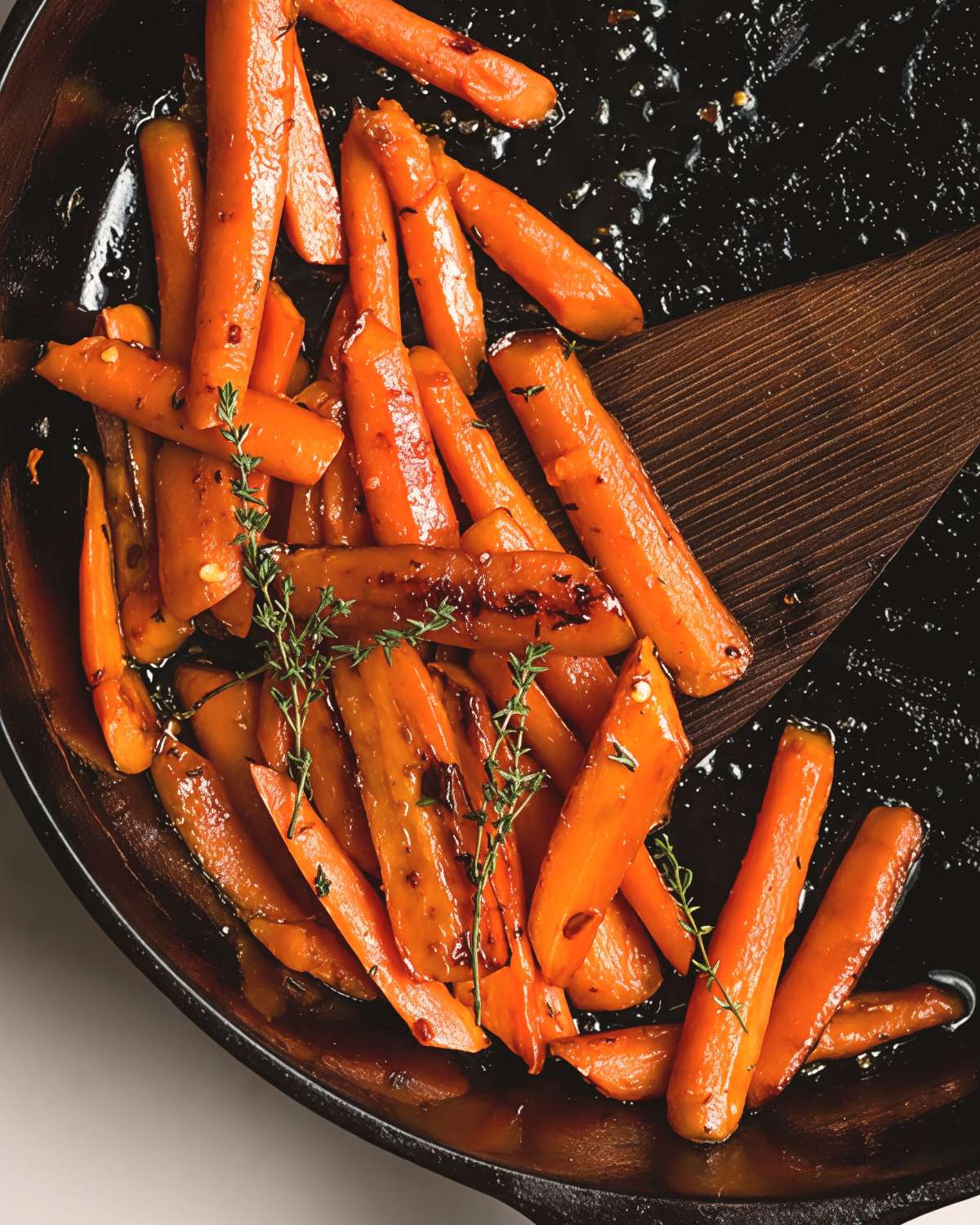 Honey sautรฉed carrots with fresh thyme in a cast-iron skillet, perfect for an easy Thanksgiving side dish.