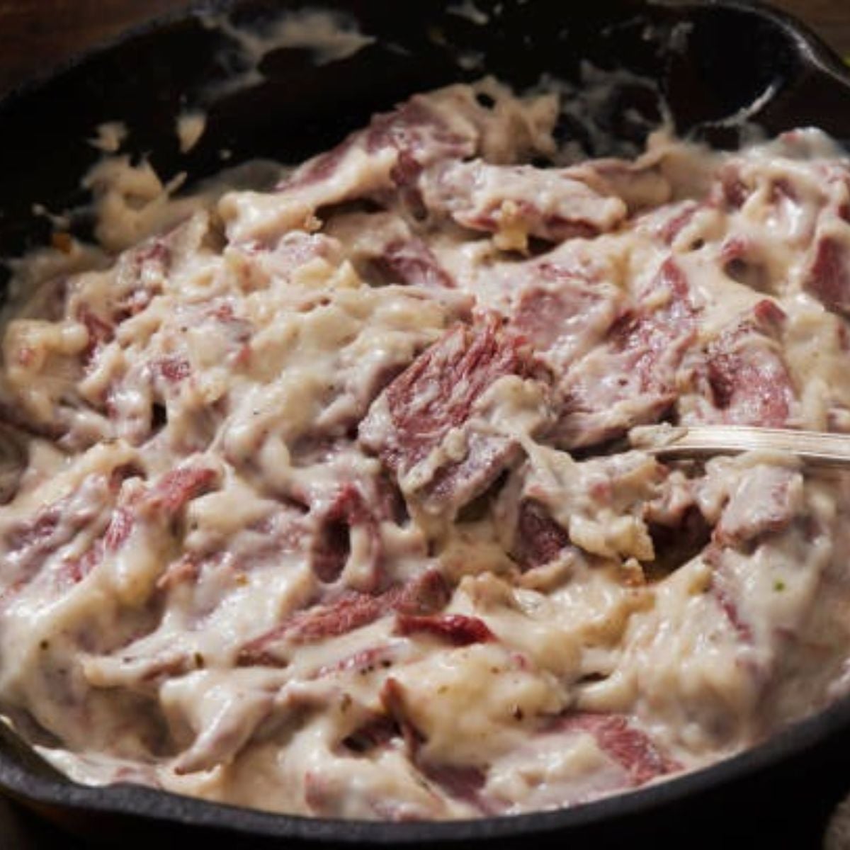 cast iron skillet filled with creamed dried beef and a silver utensil inside