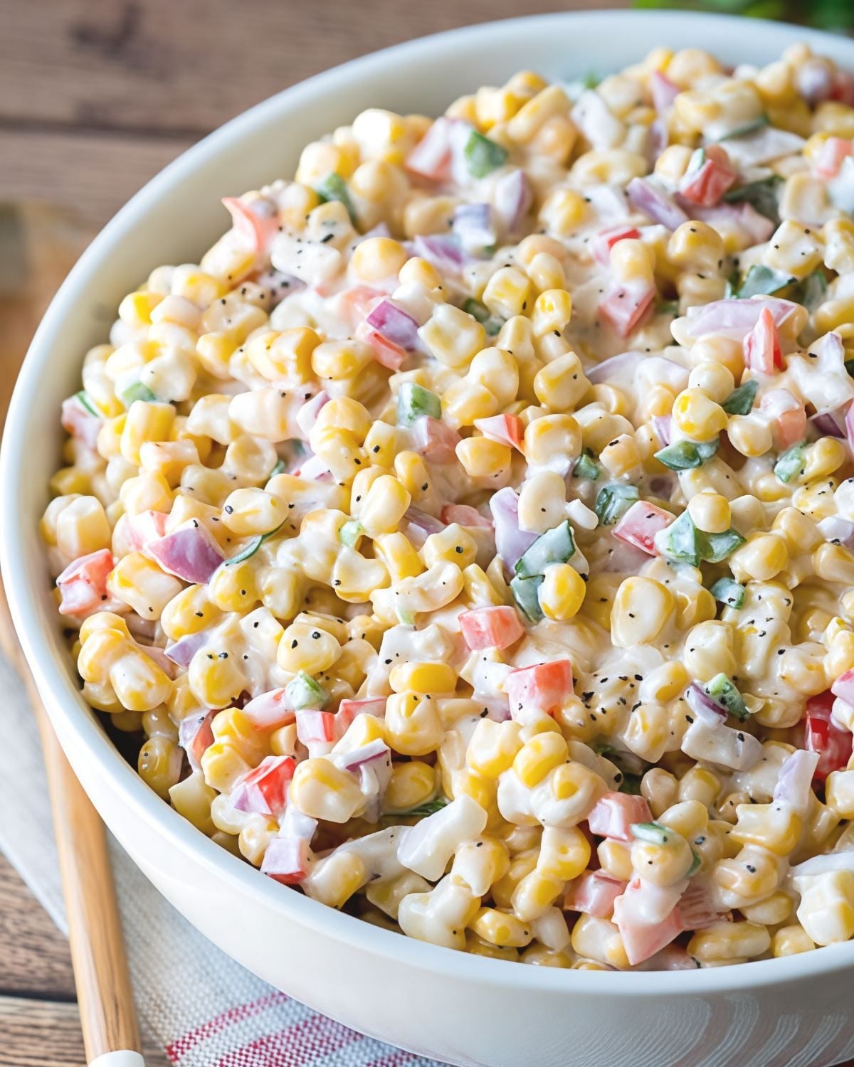 Creamy corn salad with diced peppers and red onions in a white serving bowl, a quick and easy Thanksgiving side dish.