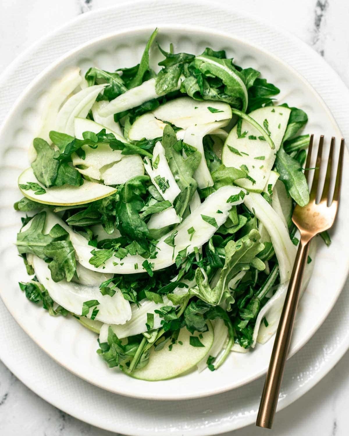 Fennel and apple salad with greens in a white bowl with a fork, served as a cold Thanksgiving side dish