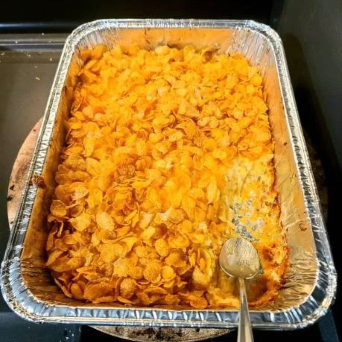 foil pan of funeral potatoes with a portion out and a sliver spoon in the pan