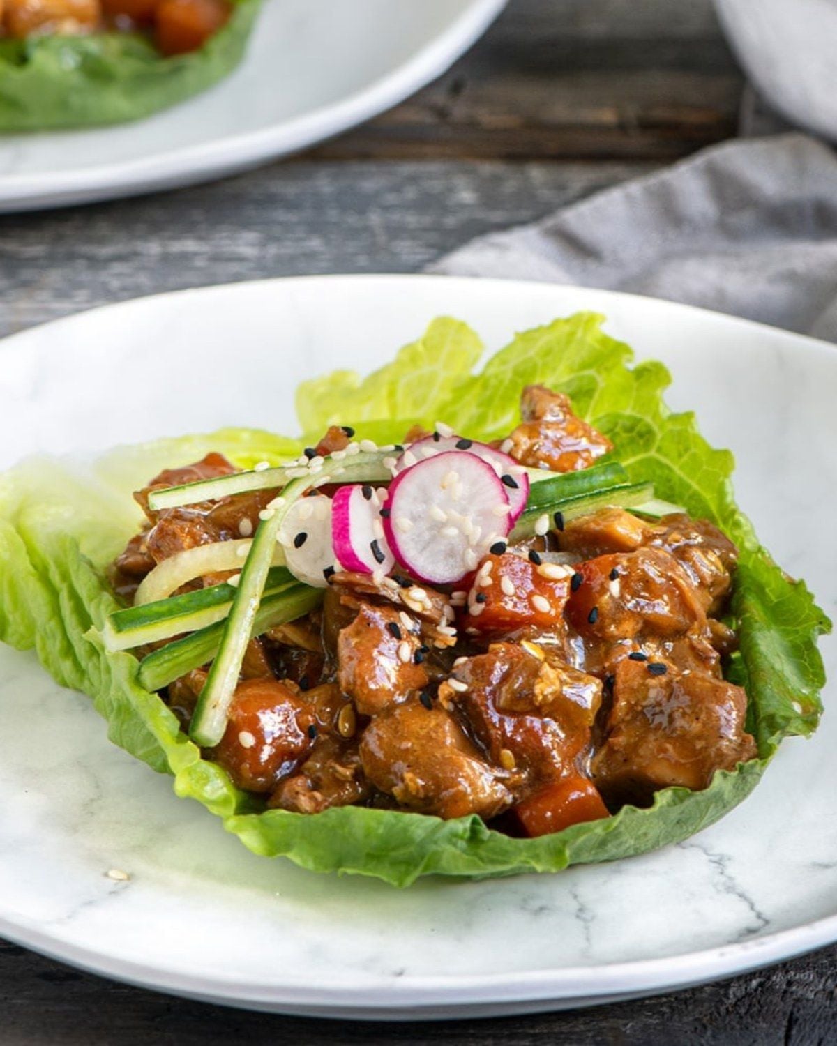 A lettuce wrap filled with diced chicken and vegetables, topped with sesame seeds and radish slices