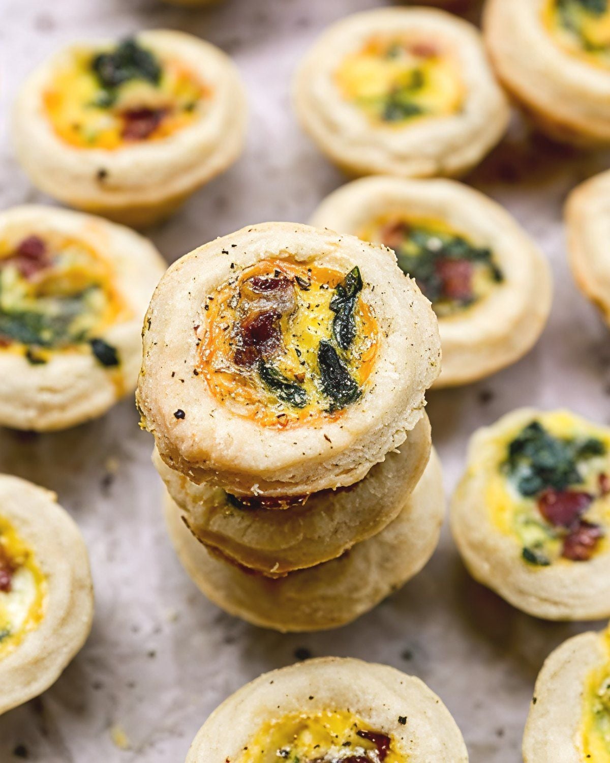 A vertical stack of baked mini quiches filled with spinach and bacon, making an easy and crowd-pleasing brunch potluck idea.
