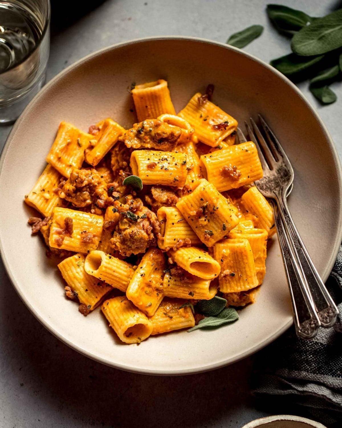 Rigatoni tubes coated in a creamy squash puree and savory meat crumbles inside a shallow bowl.