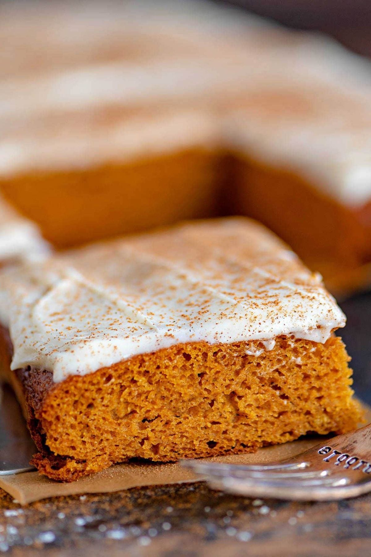 A slice of moist pumpkin sheet cake with cream cheese frosting and cinnamon dusting