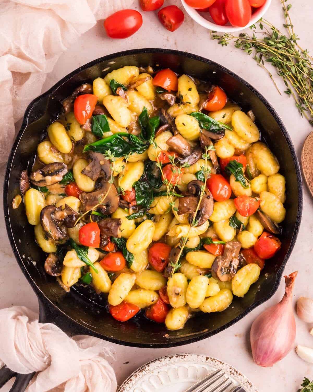 Homemade potato gnocchi sautรฉed with mushrooms, cherry tomatoes, and spinach in a cast-iron skillet