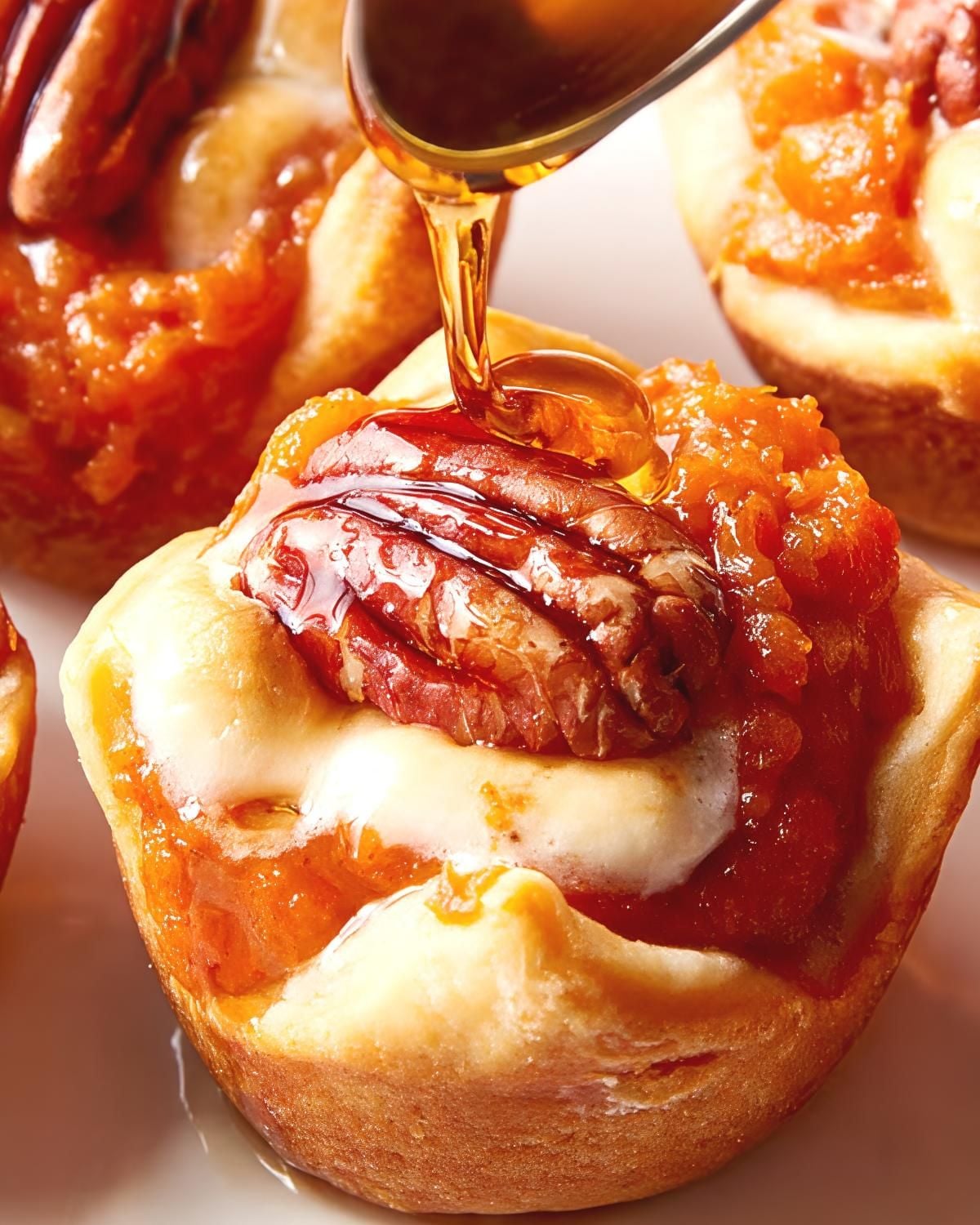Syrup being poured onto a sweet potato crescent bite topped with a pecan, perfect for Thanksgiving appetizers."
