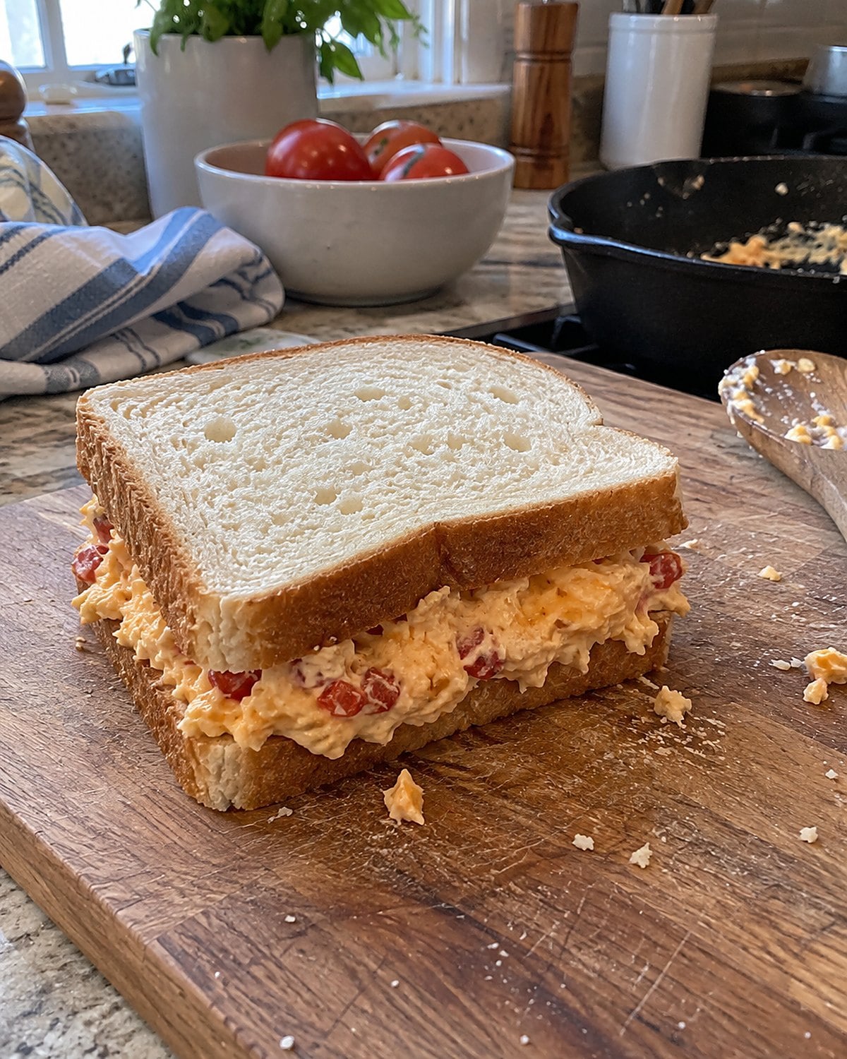 Pimento cheese between slices of white bread on a cutting board beside a cast-iron pan.