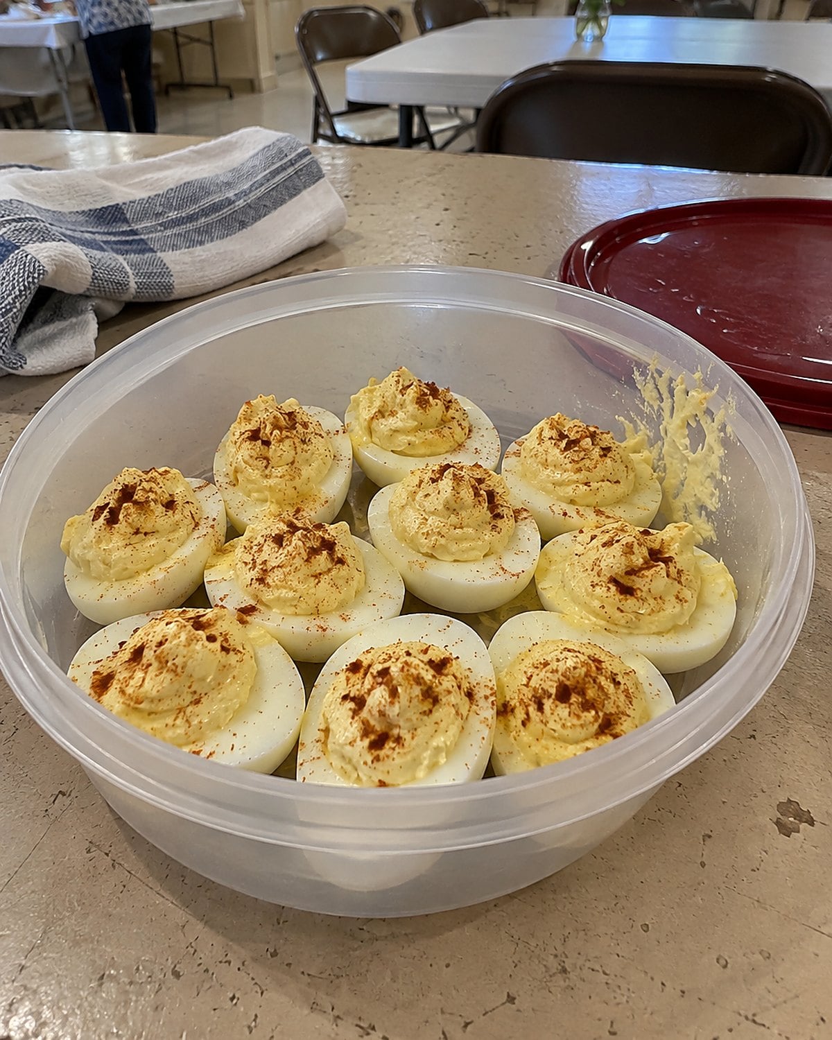 A lidded container of deviled eggs on a church hall table, with one filling slightly smudged.
