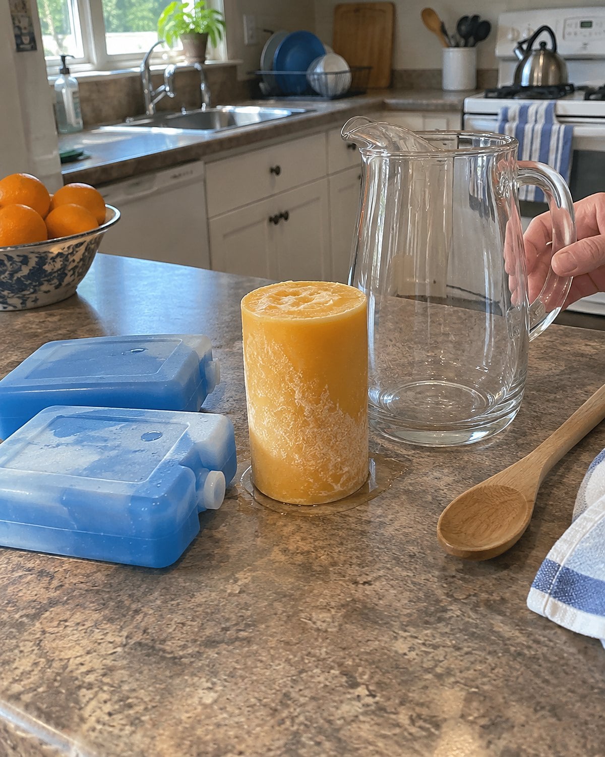 A frozen can of orange drink concentrate beside a pitcher and two ice packs on a counter.