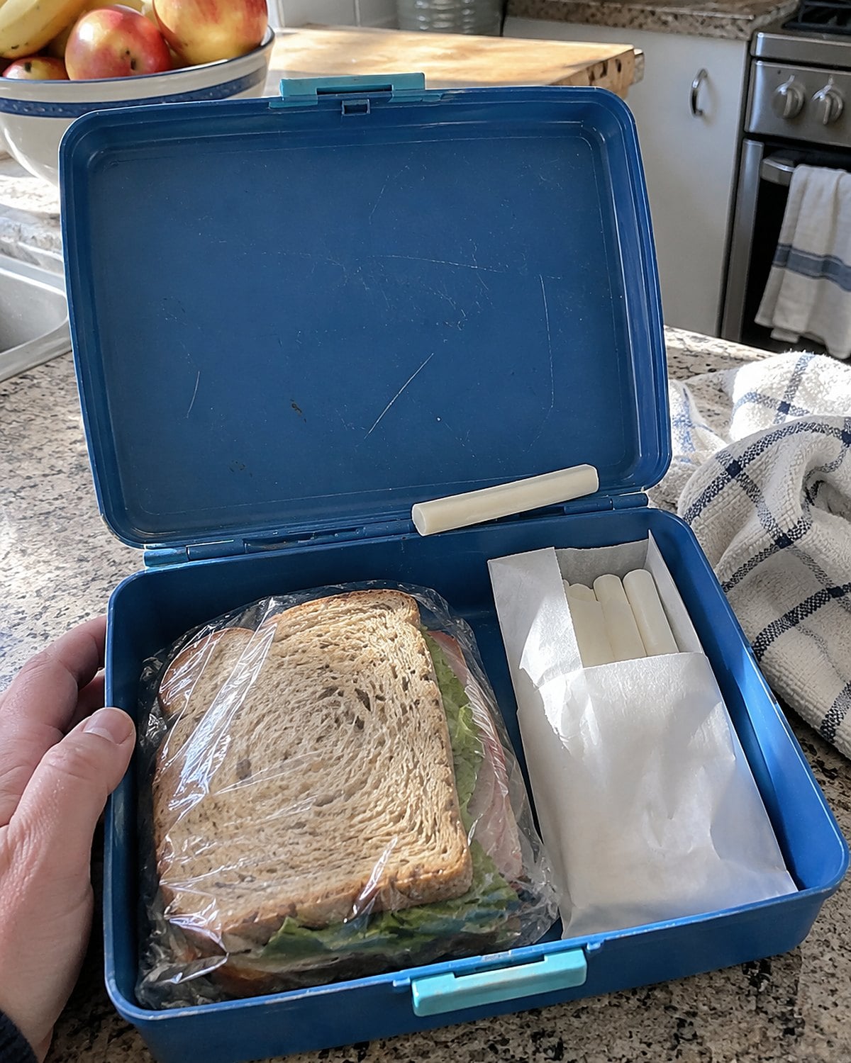A plain paper pack of white candy sticks beside a wrapped sandwich inside an open lunchbox.