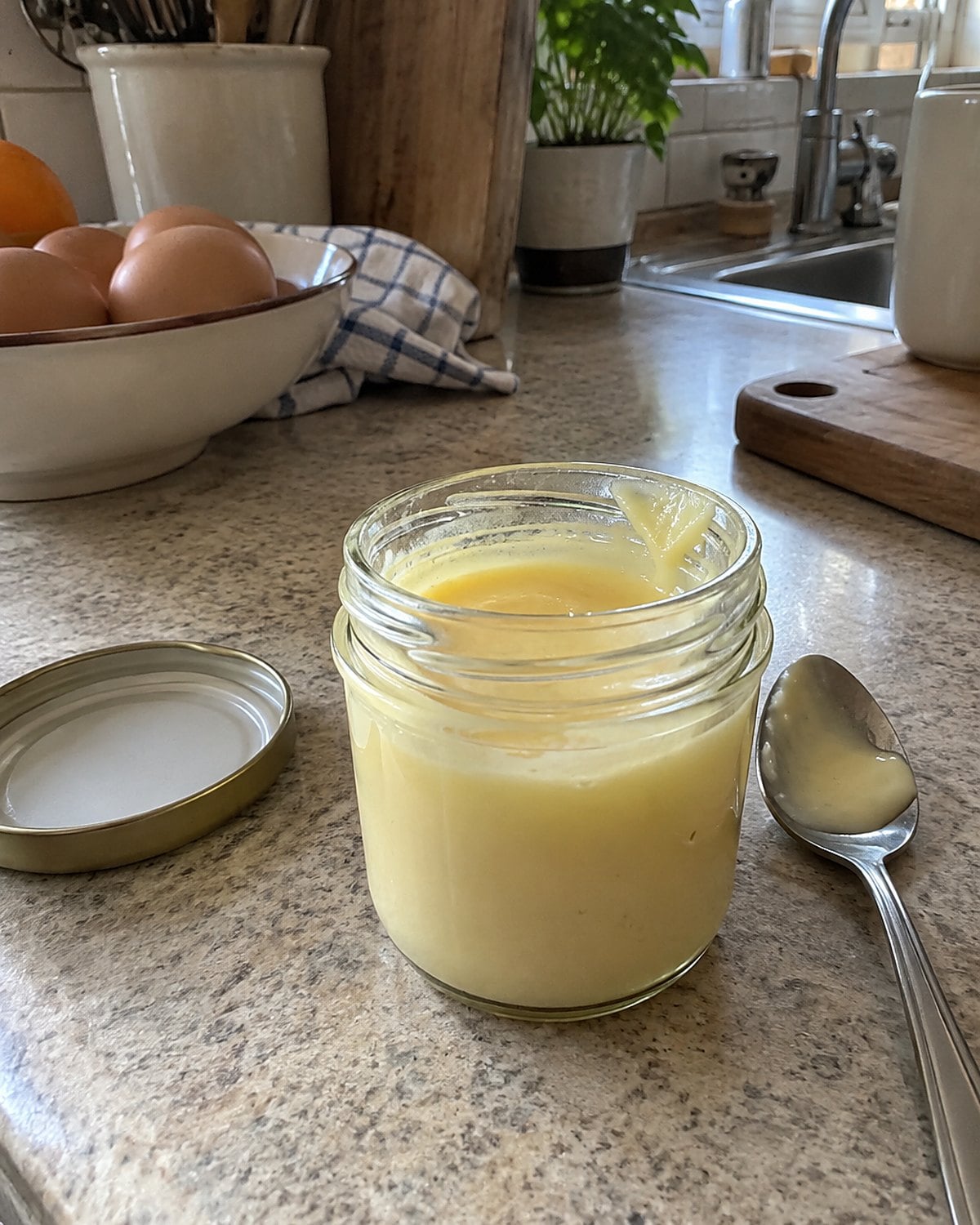 A small glass jar of homemade custard and a spoon on a kitchen counter.