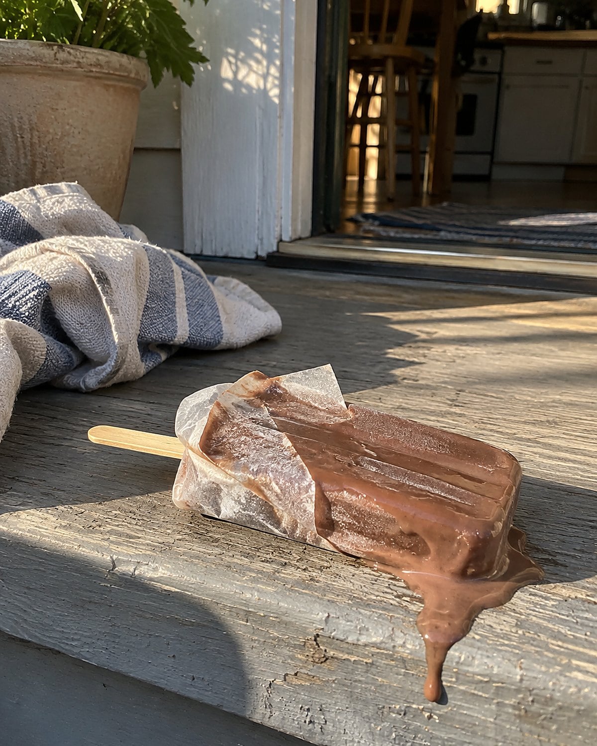 A softened homemade pudding pop in torn waxed paper on a back porch step.