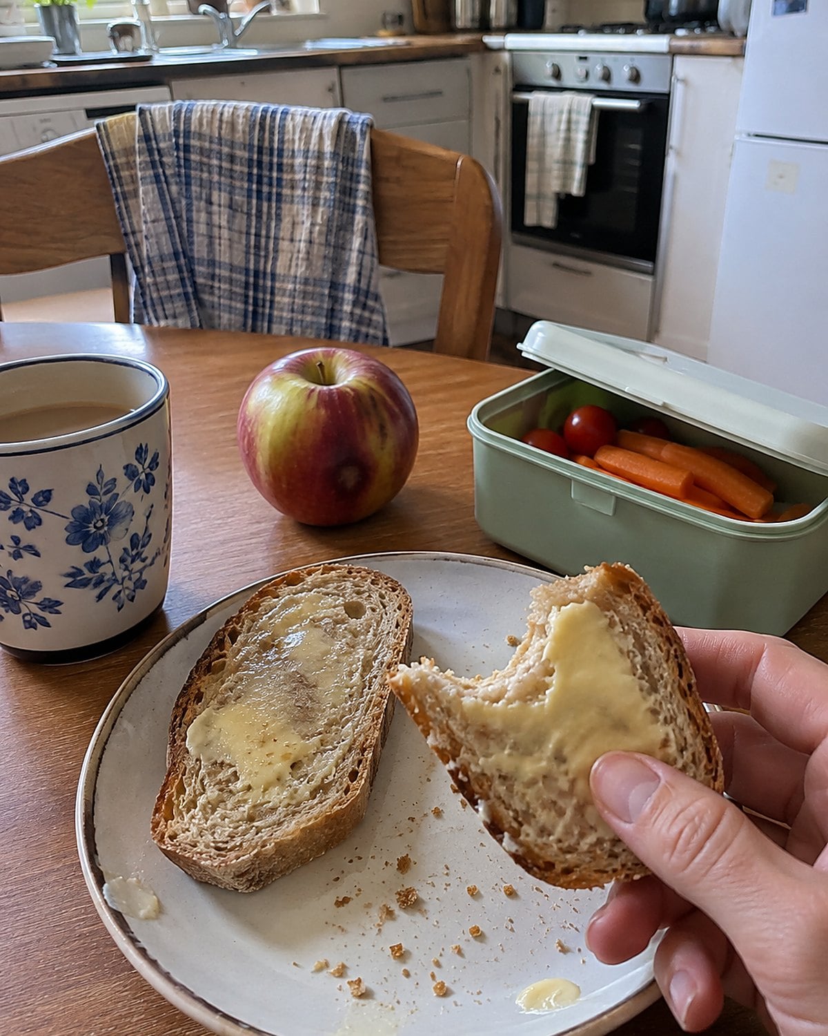 Buttered bread beside a bruised apple and a clean lunchbox on a breakfast table.