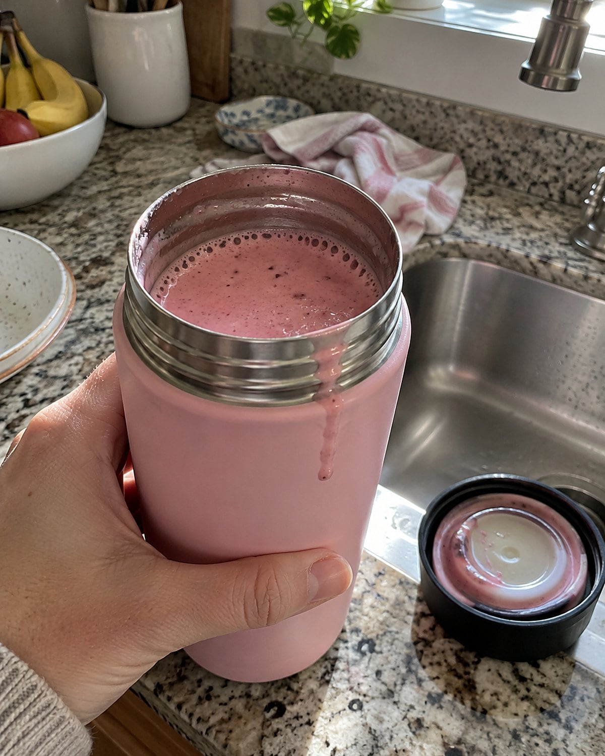 A pink drink in an open thermos beside a lid with a stained gasket at the sink.