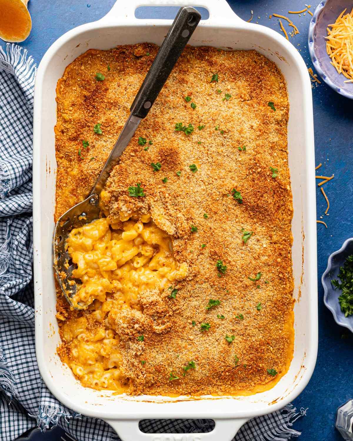 A white ceramic baking dish filled with creamy butternut squash macaroni and cheese topped with a golden breadcrumb crust, garnished with fresh parsley