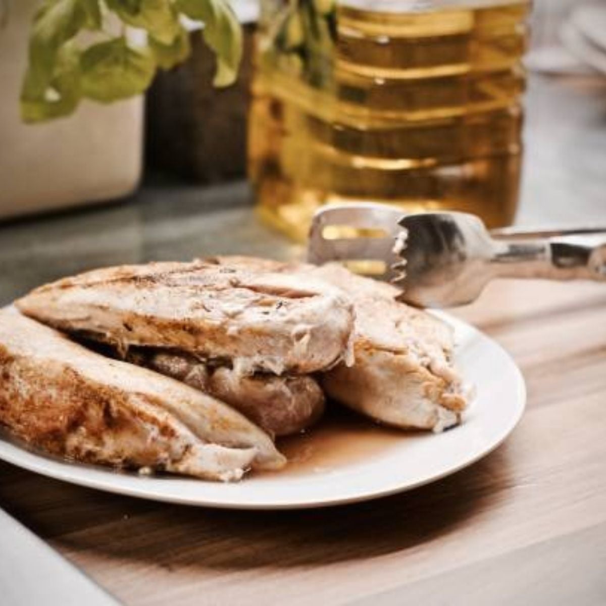 Sliced chicken on a plate with juices and a silver tongs on the side