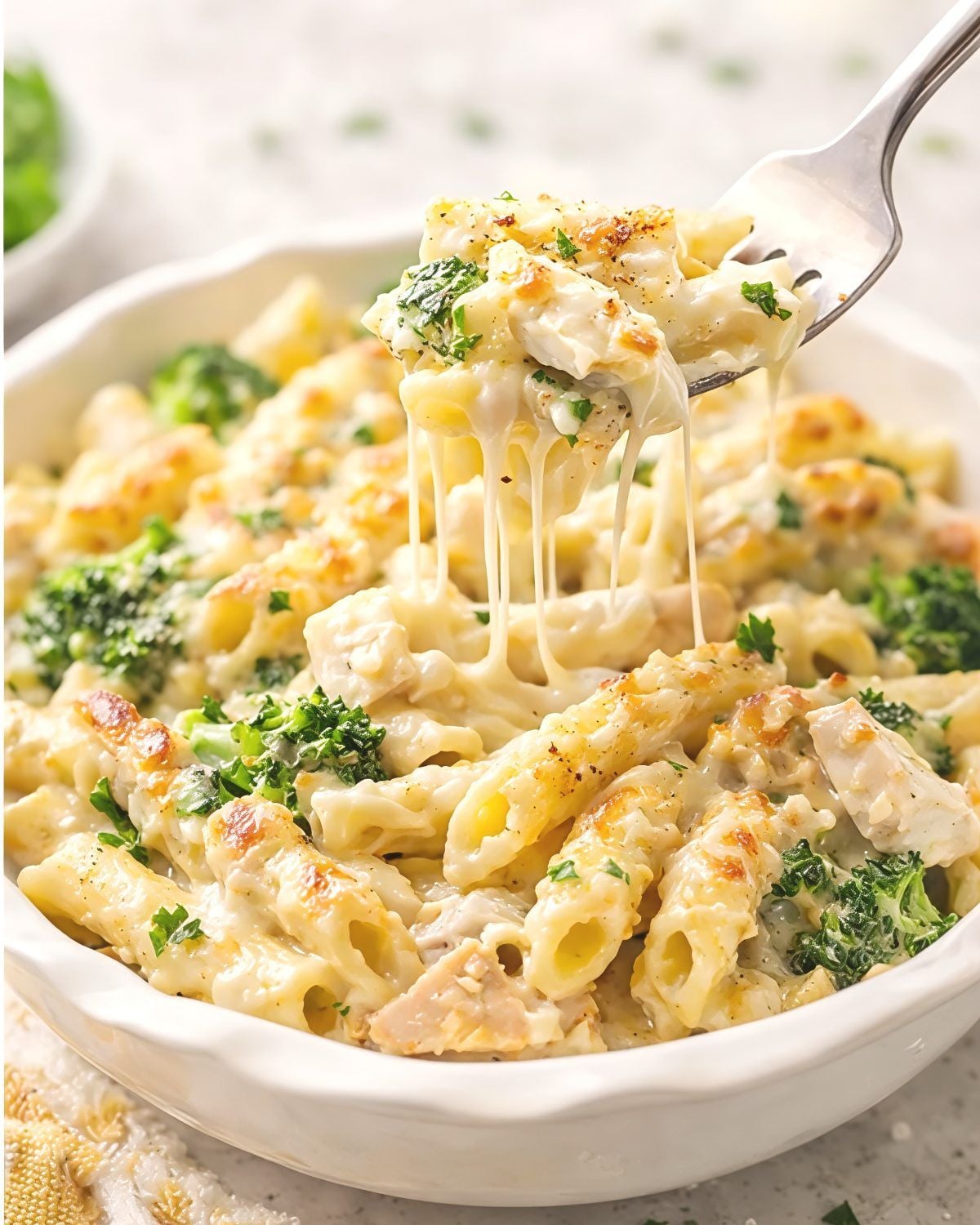 Chicken and broccoli alfredo dump and bake pasta casserole in a white bowl with stretchy melted cheese on a fork