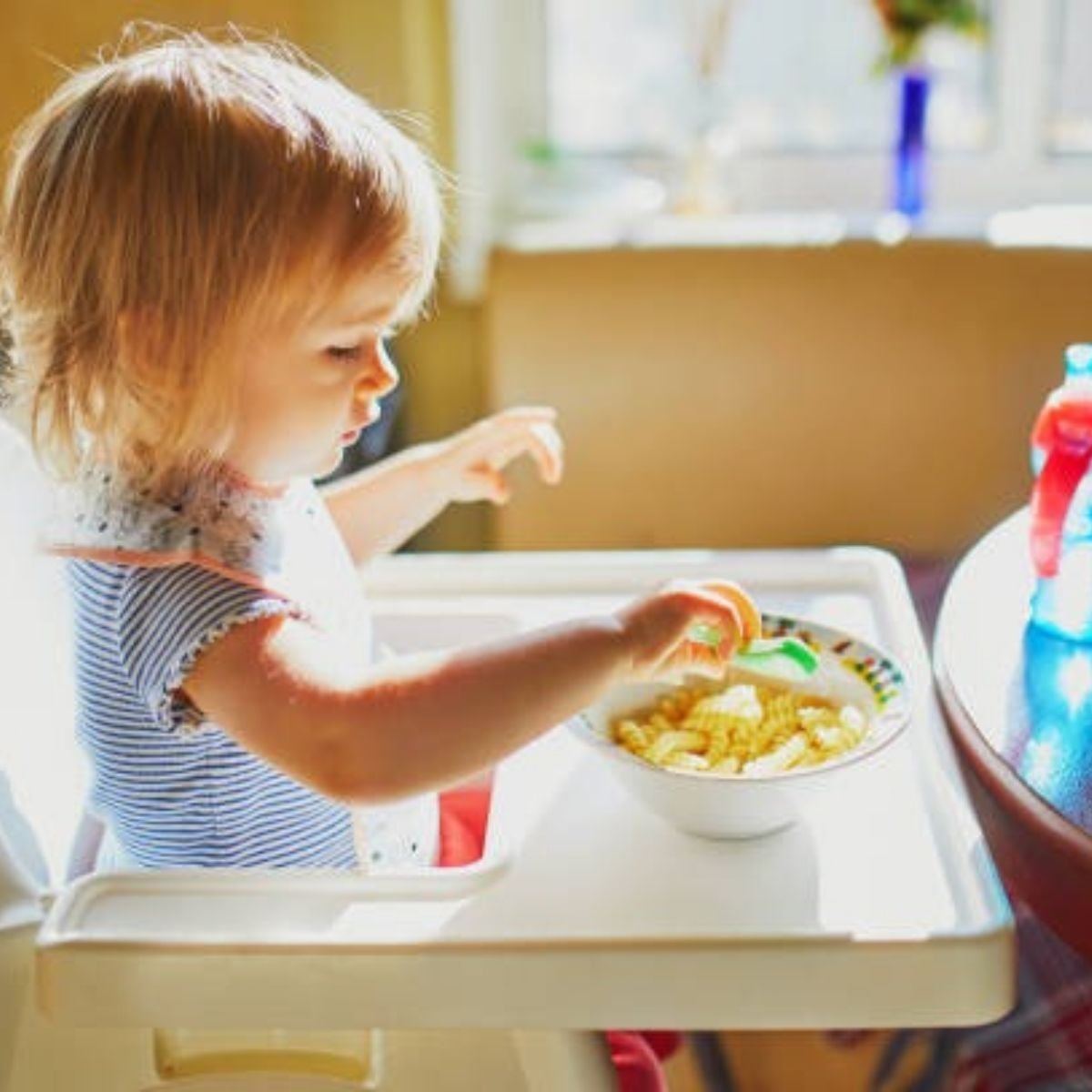 A little girl using her hands to eat macaroni