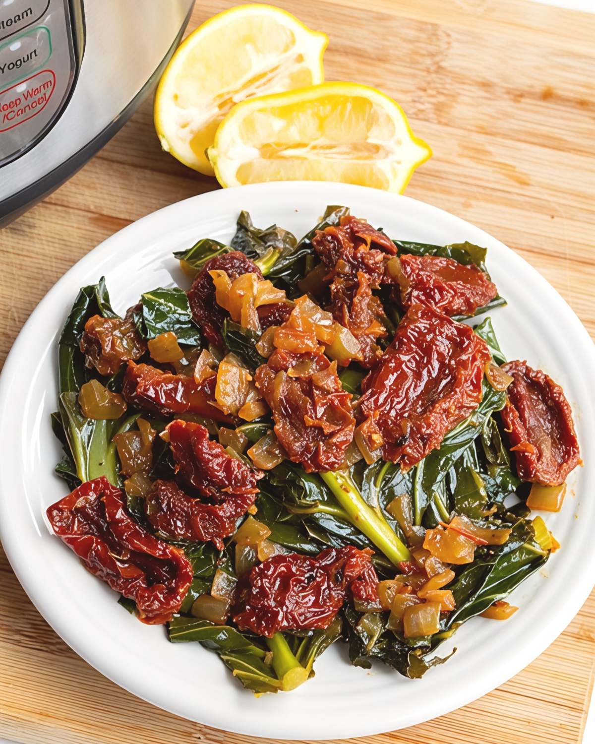 Tender collard greens sautรฉed with sun-dried tomatoes and onions are served on a white plate next to lemon wedges and an Instant Pot.