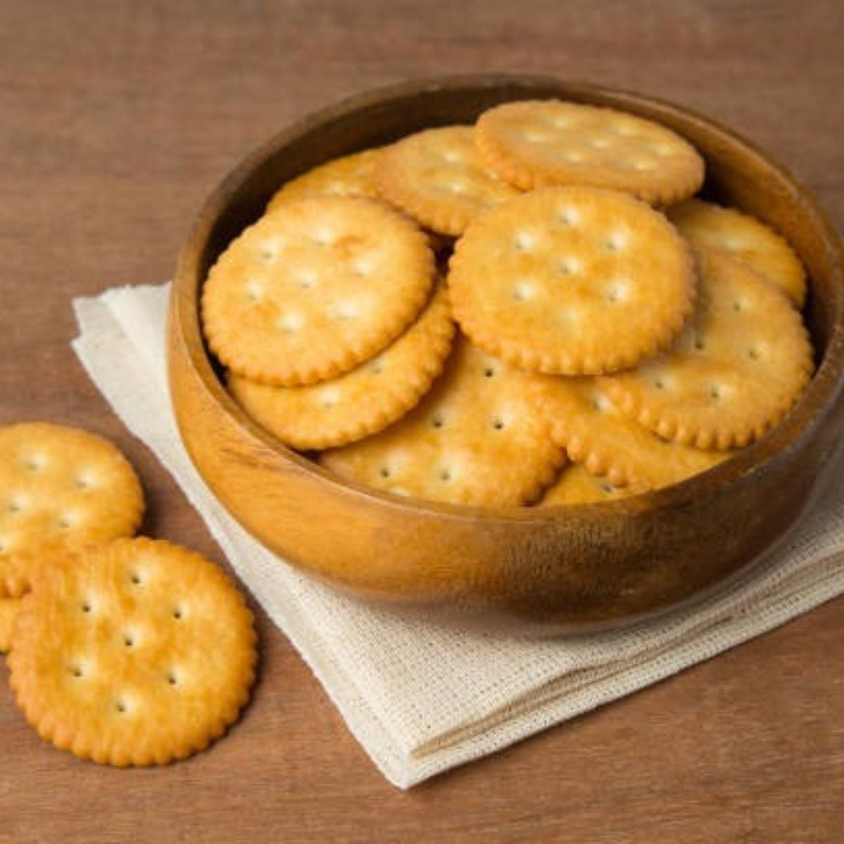 Ritz crackers in a wooden bowl on top of serviettes and a wooden counter