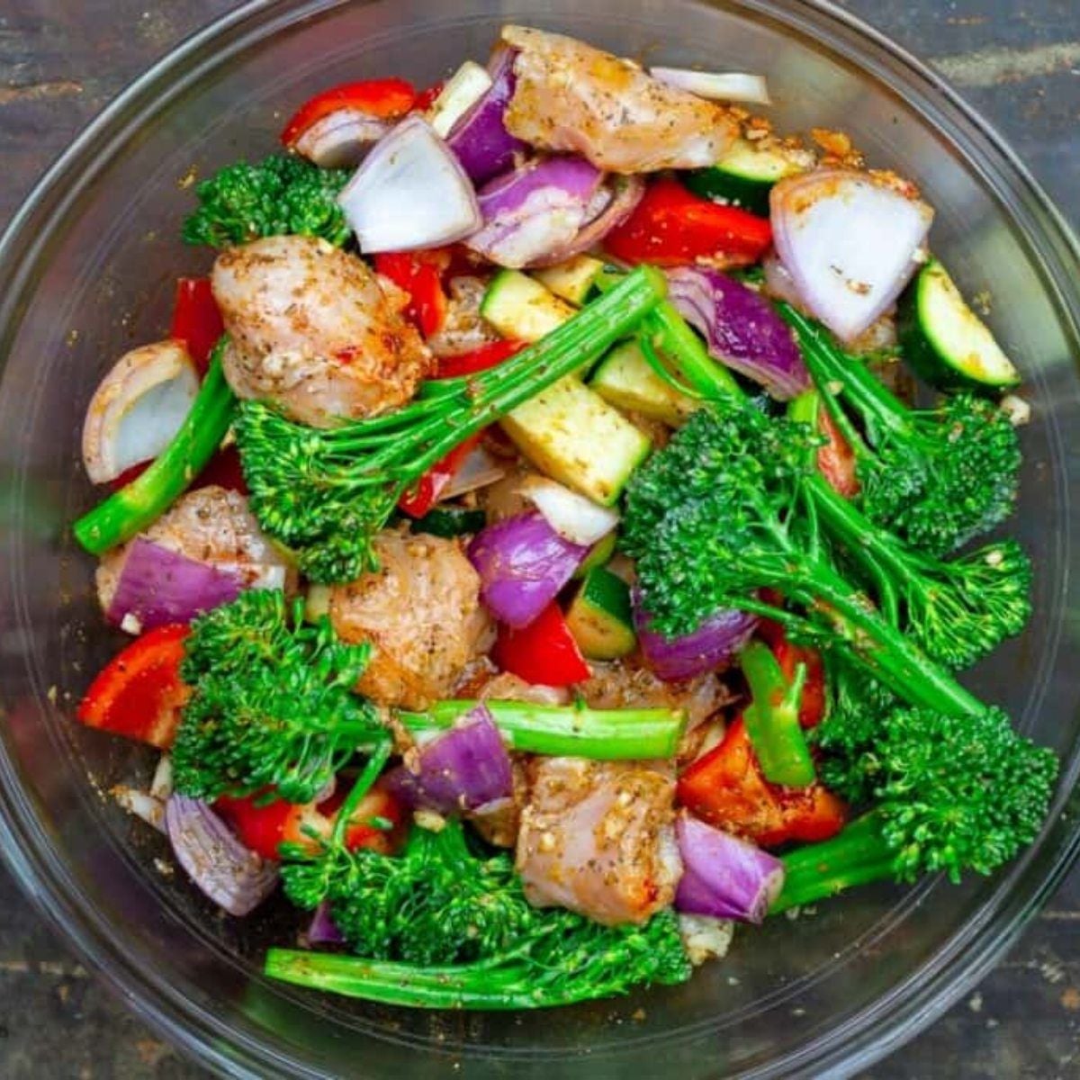 Sheet pan chicken and vegetables ready for dump and bake cooking in a glass bowl.
