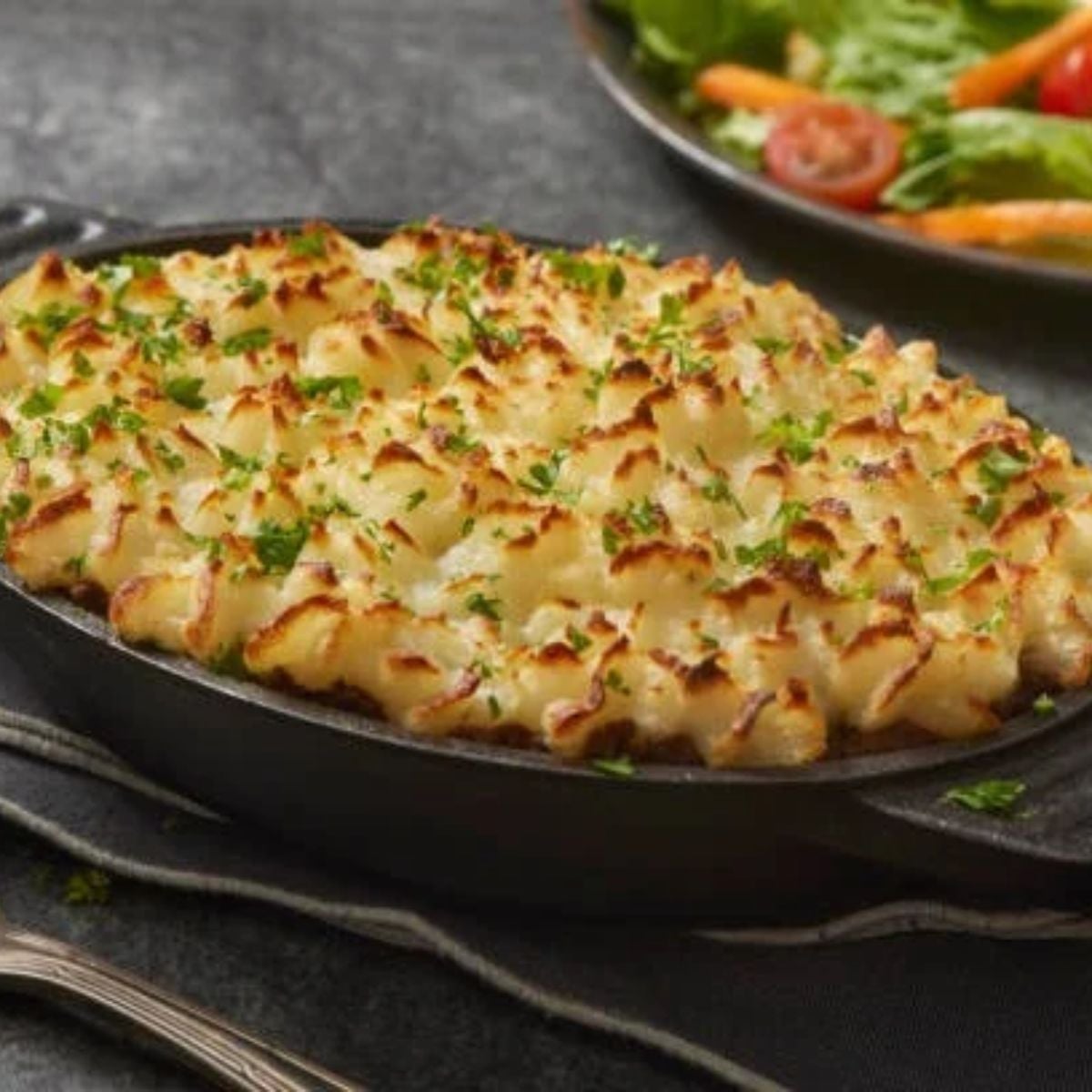 Shepherd’s Pie Under Mashed Potatoes in a black casserole dish with a salad on the side