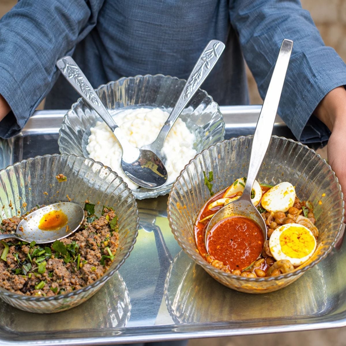 Various dishes of half eaten food on a silver tray with serving spoons inside the dishes