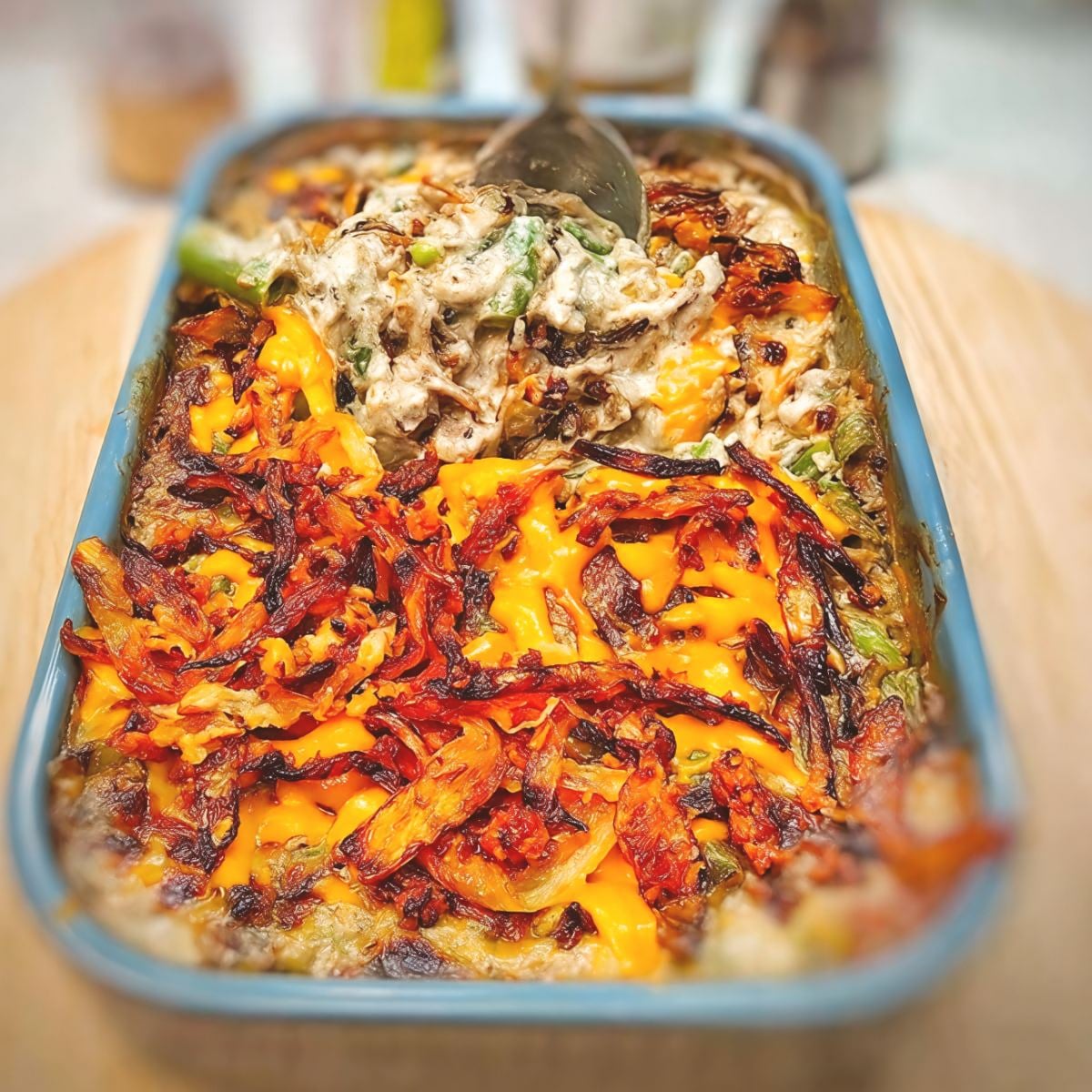 A baking dish filled with creamy air fryer green bean casserole topped with melted cheddar cheese and crispy fried onions, making a classic Thanksgiving vegetable side dish.