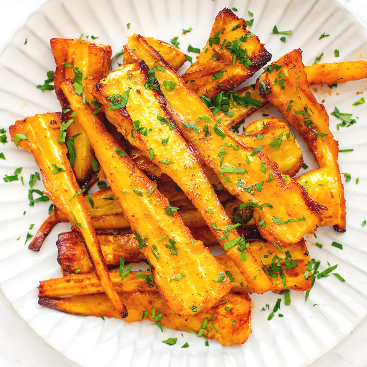 Crispy air fryer parsnip wedges seasoned and garnished with fresh parsley on a white plate, served as one of the best gluten-free Thanksgiving side dishes.
