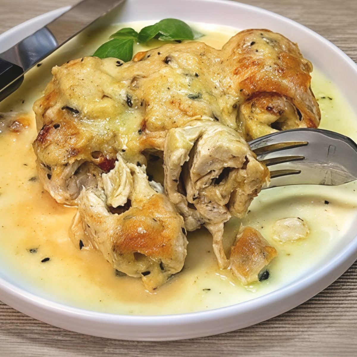 A sliced portion of juicy Air Fryer Stuffed Chicken Breast Roll-Ups held on a fork over a creamy herb sauce, featured as a delicious high protein low carb recipes dinner.