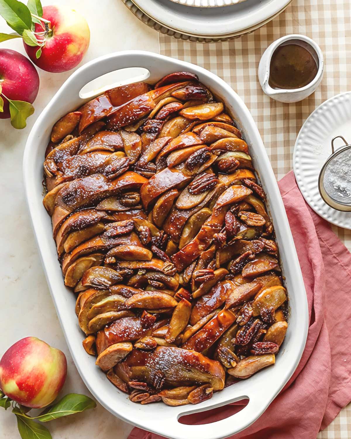A baking dish filled with baked apple cider french toast casserole topped with sliced apples and pecans as Thanksgiving breakfast ideas.